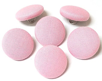 May include: Six pink fabric covered buttons with a silver shank. The buttons are round and have a slightly textured surface.