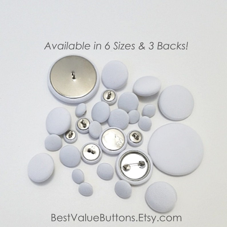 May include: A collection of white fabric-covered buttons in various sizes, with metal backs. Some buttons have a pin back, while others have a loop or shank. The text "Available in 6 Sizes & 3 Backs!" is visible.