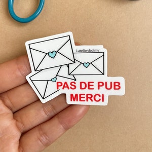 Stop pub mignon avec 3 enveloppes blanches fermées par des cœurs bleus. En bas à droite, on peut lire le textes écrit en rouge «pas de pub merci ». L’autocollant a un fini mat.