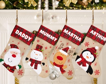 May include: Four beige burlap Christmas stockings with red and black plaid cuffs. Each cuff features a white name: DADDY, MUMMY, MARTHA, and ARTHUR. The stockings are decorated with felt appliques of a Santa, a snowman, a reindeer, and a penguin.