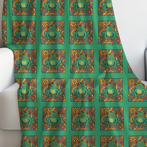 May include: A green throw blanket draped over a white armchair. The blanket features a repeating pattern of green, yellow, orange, and red stylized frog designs within square frames. The background is a solid green.