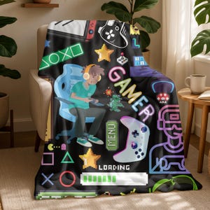 May include: Black blanket with a gamer theme, featuring a cartoon gamer, game controllers, stars, and the word "GAMER" in neon colors. The blanket has a pixelated design with a loading bar and game console icons.