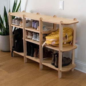 Könnte beinhalten: Ein Schuhregal aus Holz mit fünf Ablagen, auf denen Schuhe, Stiefel und Rucksäcke stehen. Das Regal ist aus hellem Holz und hat eine abgerundete Kante an der oberen Ablage.