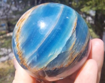 May include: A blue and brown banded sphere of polished blue calcite. The sphere is smooth and has a high gloss finish.