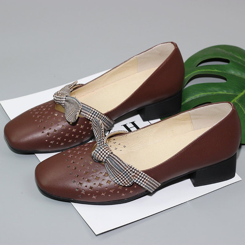 Puede incluir: Zapatos de cuero marr&oacute;n con tac&oacute;n bajo de bloque y detalle de lazo de cuadros. Los zapatos tienen un dise&ntilde;o perforado y una punta redonda.