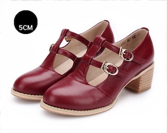 May include: A pair of burgundy leather heeled shoes with double buckles and a t-strap design. The heels are approximately 5 cm high.