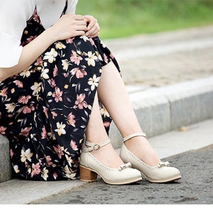 May include: A woman wearing a floral print dress and white shoes with ankle straps. The shoes have a small bow on the toe.