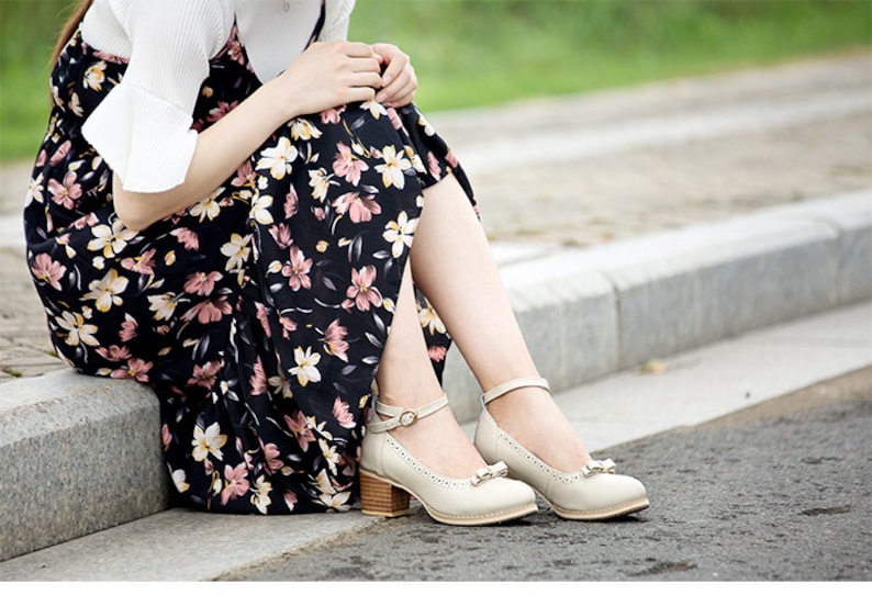 May include: A woman wearing a floral print dress and white shoes with ankle straps. The shoes have a small bow on the toe.