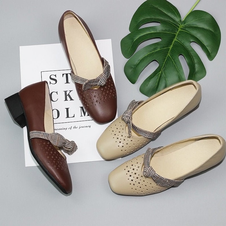 Puede incluir: Dos pares de zapatos de mujer con lazos. Un par es marr&oacute;n con un tac&oacute;n de bloque y el otro par es beige con un tac&oacute;n plano. Ambos pares tienen un patr&oacute;n a cuadros en los lazos y est&aacute;n hechos de cuero.