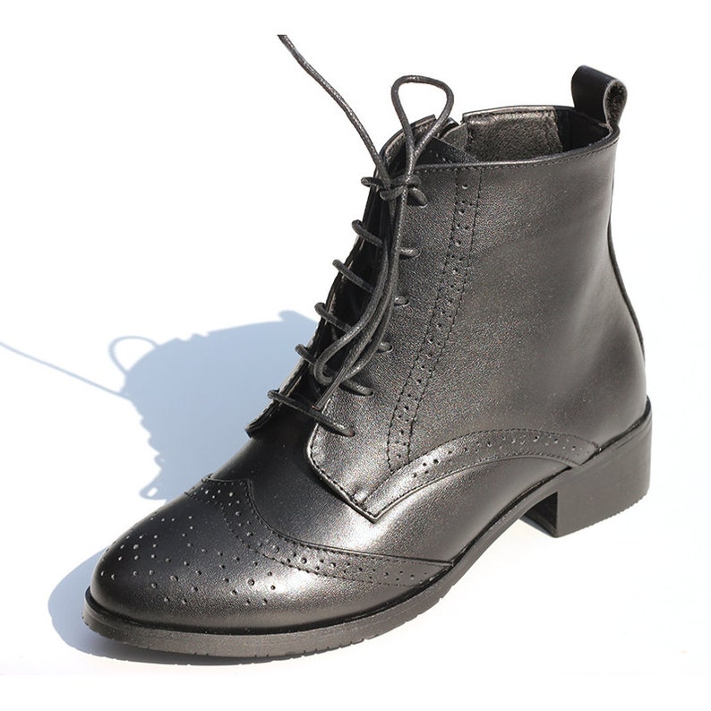 May include: Black leather ankle boots with lace-up closure and a brogue design. The boots have a low block heel.