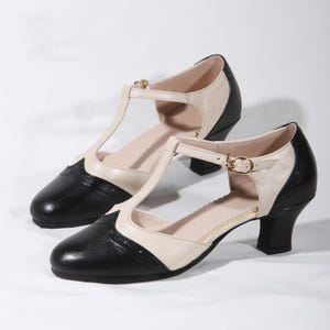 Peut inclure: Chaussures à talons bicolores noir et blanc avec une bride en T et une fermeture à boucle. Les chaussures ont une pointe pointue et un talon bloc bas.