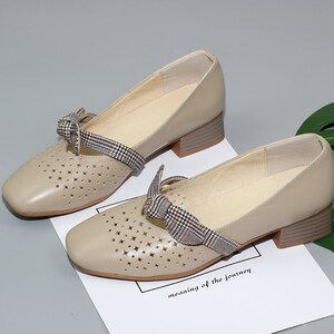 Puede incluir: Zapatos de cuero beige con un lazo de cuadros y detalles recortados. Los zapatos tienen un tac&oacute;n bajo de bloque.
