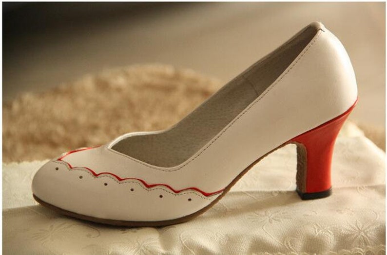 Pu&ograve; includere: Scarpa bianca con tacco alto con un bordo rosso attorno al bordo della punta e un tacco rosso.