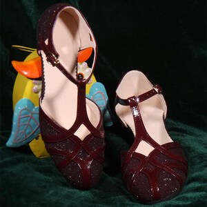 May include: A pair of burgundy T-strap sandals with a sparkly finish. The sandals have a low heel and an open toe.
