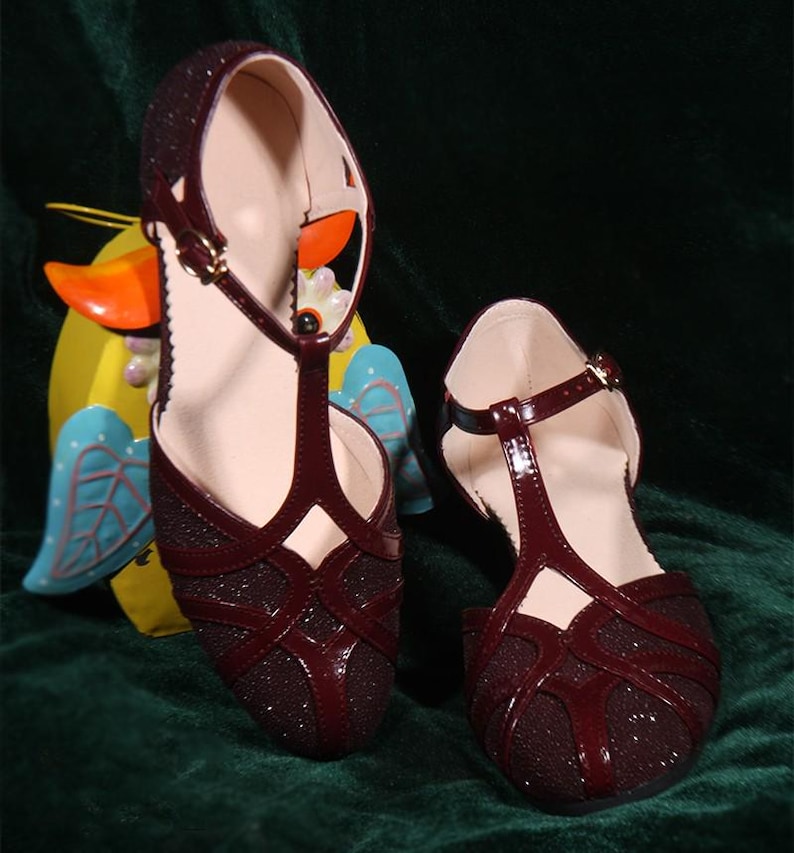 May include: A pair of burgundy T-strap sandals with a sparkly finish. The sandals have a low heel and an open toe.