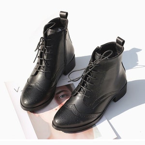 May include: Black leather ankle boots with lace-up closure and a brogue design. The boots have a low block heel and a side zipper.