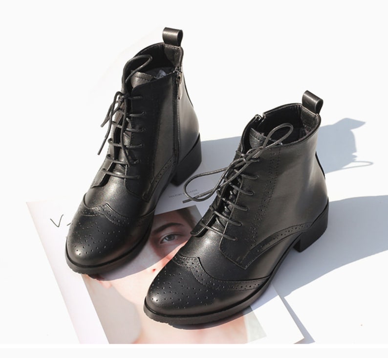 May include: Black leather ankle boots with lace-up closure and a brogue design. The boots have a low block heel and a side zipper.