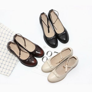 May include: Three pairs of ankle strap shoes with bows on the toe. The shoes are in black, brown, and cream.