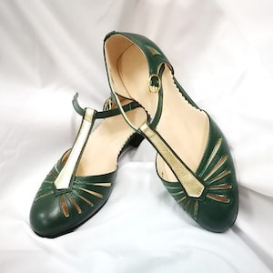 Pu&ograve; includere: Un paio di scarpe in pelle verde con dettagli dorati e tagli. Le scarpe hanno un design a cinturino a T e un tacco basso.
