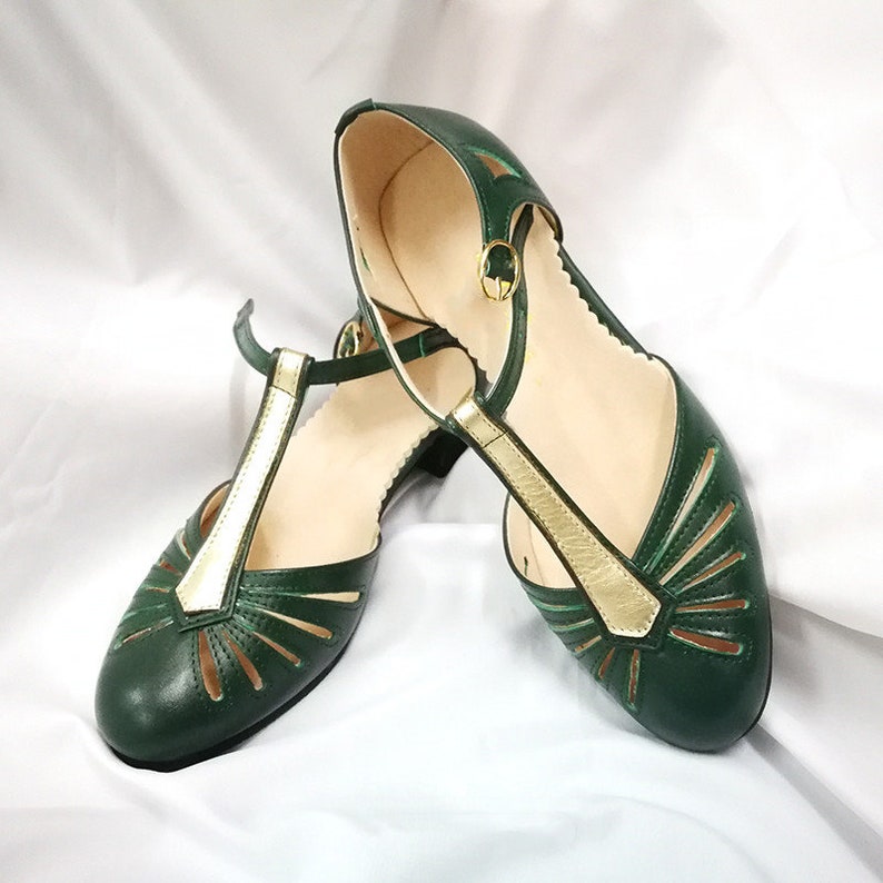 Pu&ograve; includere: Un paio di scarpe in pelle verde con dettagli dorati e tagli. Le scarpe hanno un design a cinturino a T e un tacco basso.