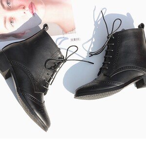 May include: A pair of black leather ankle boots with lace-up closures and a brogue design. The boots have a low block heel.