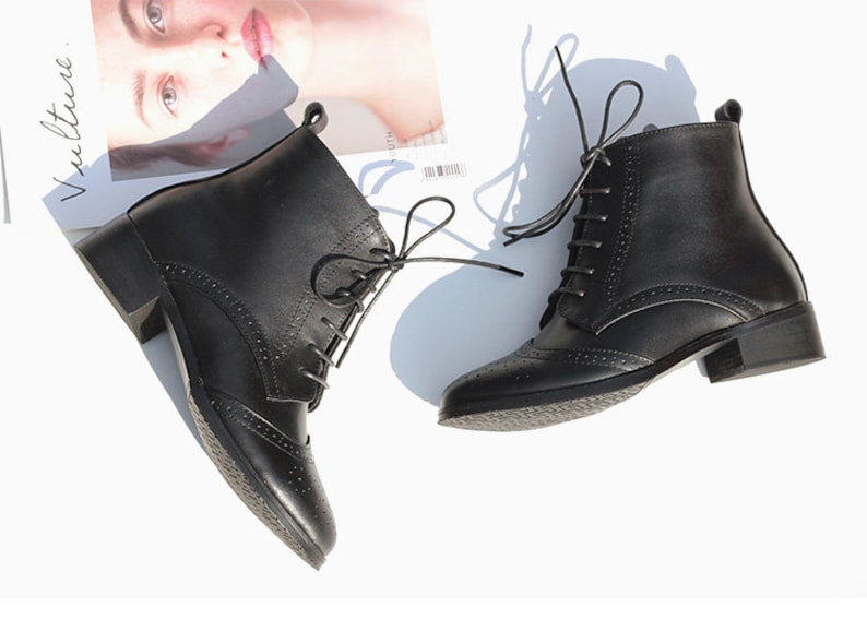 May include: A pair of black leather ankle boots with lace-up closures and a brogue design. The boots have a low block heel.