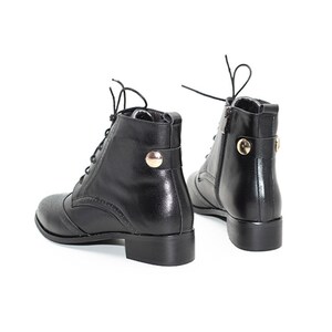 May include: Black leather ankle boots with lace-up closures and gold accents. The boots have a rounded toe and a low block heel.