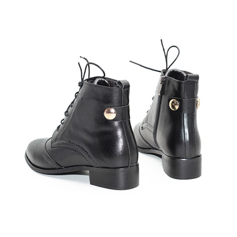 May include: Black leather ankle boots with lace-up closures and gold accents. The boots have a rounded toe and a low block heel.