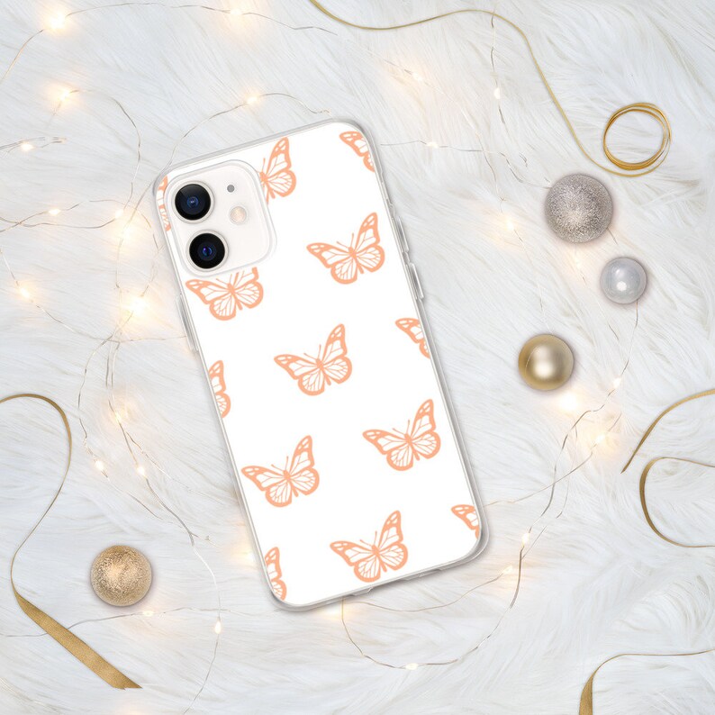 Puede incluir: Una funda transparente para tel&eacute;fono con fondo blanco y un patr&oacute;n repetido de mariposas de color melocot&oacute;n.