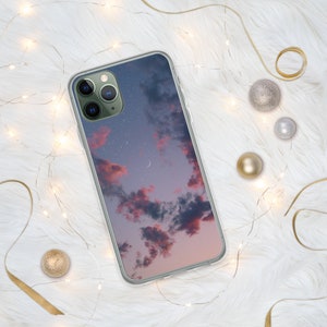 May include: A clear phone case with a pink and purple sunset sky with stars and a crescent moon printed on it.