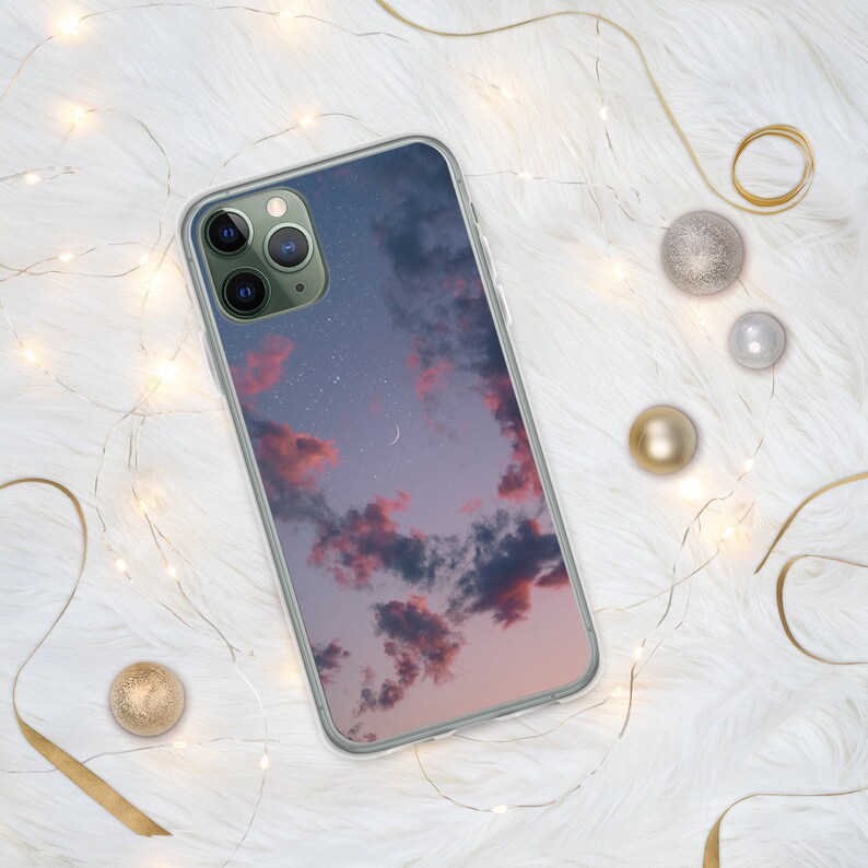 May include: A clear phone case with a pink and purple sunset sky with stars and a crescent moon printed on it.