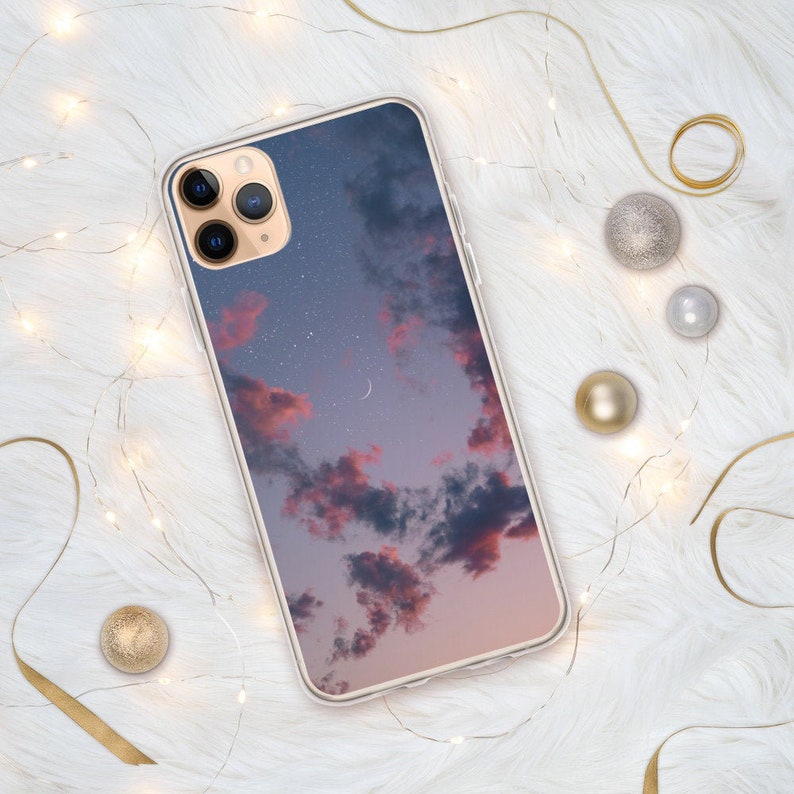 May include: A clear phone case with a pink and blue sky with stars and a crescent moon printed on it.