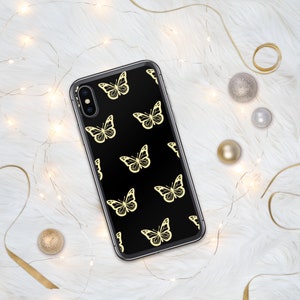 Puede incluir: Una funda de tel&eacute;fono negra con un patr&oacute;n de mariposas doradas. La funda est&aacute; hecha de pl&aacute;stico transparente y tiene un fondo negro.