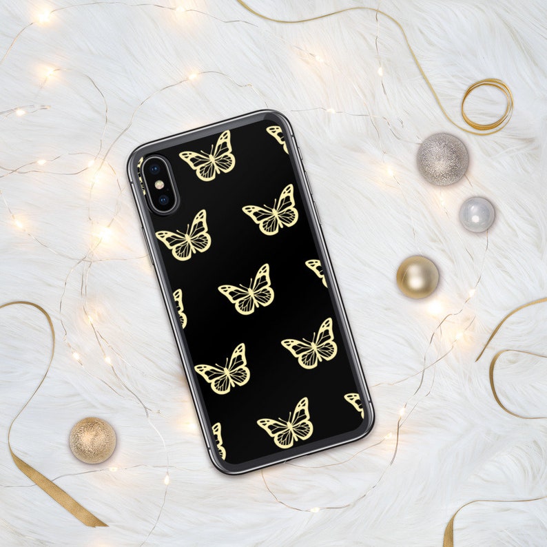Puede incluir: Una funda de tel&eacute;fono negra con un patr&oacute;n de mariposas doradas. La funda est&aacute; hecha de pl&aacute;stico transparente y tiene un fondo negro.