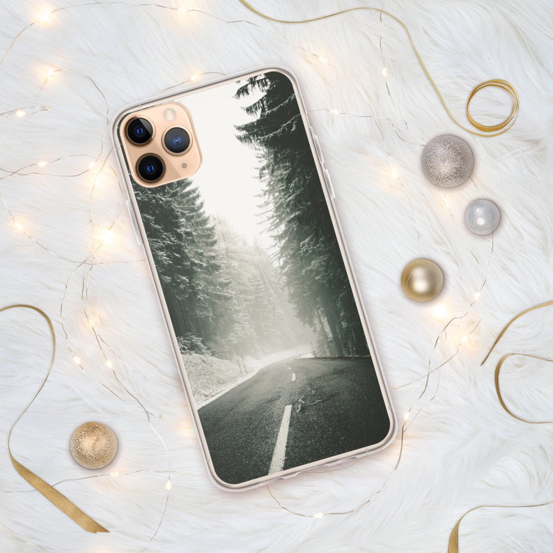 Op de afbeelding: Een transparante telefoonhoes met een winters boslandschap. De afbeelding toont een weg die door een besneeuwd bos slingert met hoge bomen aan beide kanten. De hoes heeft een zwarte camera lens uitsparing.