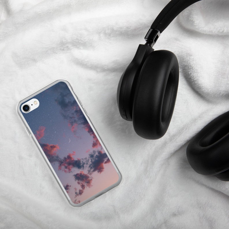 May include: A clear phone case with a pink and blue sky with clouds and stars printed on it. A pair of black headphones are also in the image.