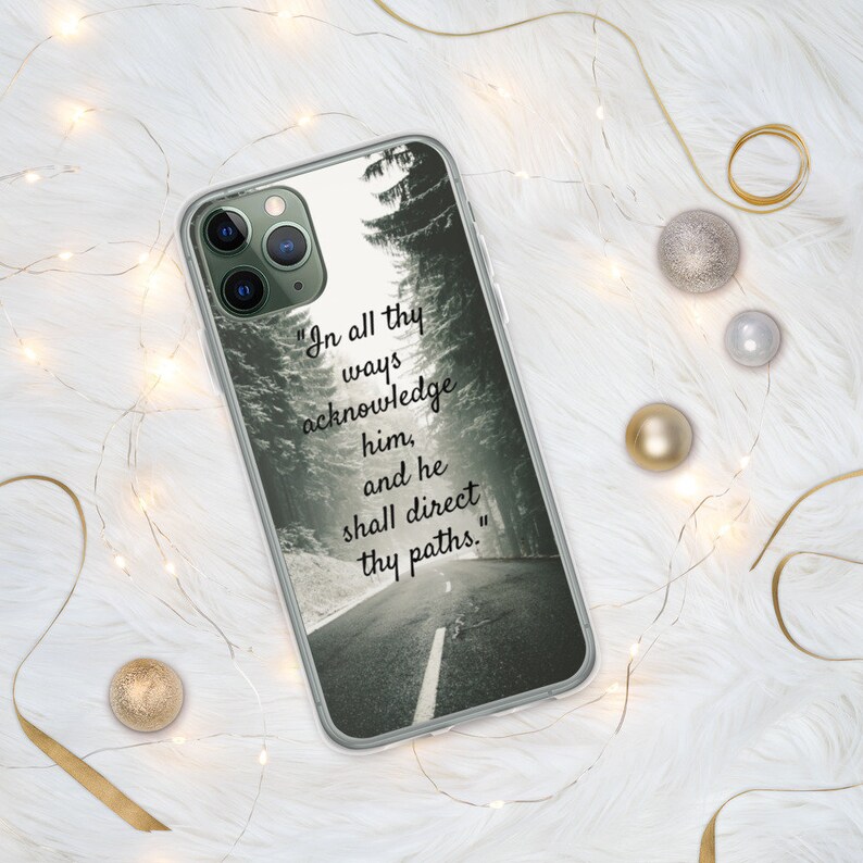 Op de afbeelding: Een transparante telefoonhoes met een zwart-witfoto van een weg door een bos. De tekst "In all thy ways acknowledge him, and he shall direct thy paths." staat op de hoes gedrukt.