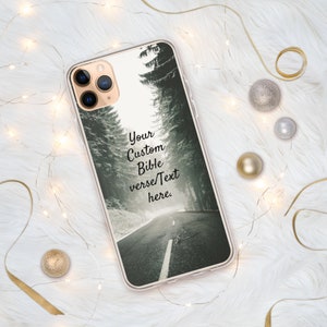 Op de afbeelding: Een transparante telefoonhoes met een zwart-witfoto van een besneeuwde weg door een bos. De tekst "Your Custom Bible verse/Text here." staat op de hoes gedrukt.