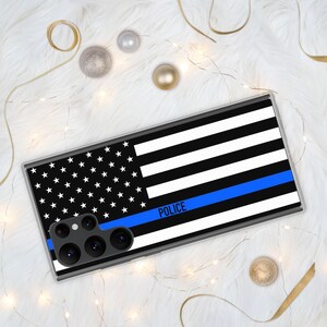 May include: A clear phone case with a black and white American flag design and a blue stripe with the word "POLICE" printed on it.