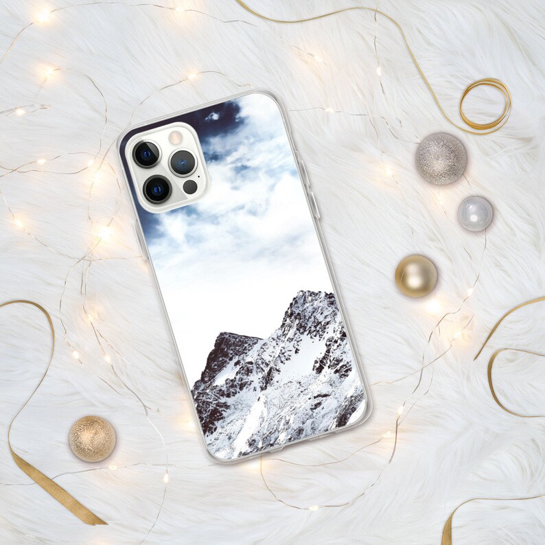 May include: A clear phone case with a snowy mountain scene printed on the back. The case is designed for an iPhone with a triple camera lens.