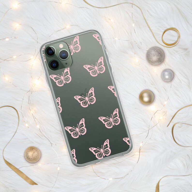 Puede incluir: Una funda transparente para tel&eacute;fono con fondo verde oscuro y un patr&oacute;n de mariposas rosas. La funda est&aacute; dise&ntilde;ada para un iPhone con una c&aacute;mara de triple lente.