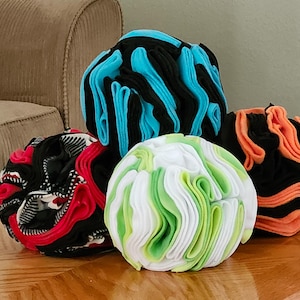 May include: Four fabric balls, each made of multiple layers of fabric, in different colors and patterns. The balls are arranged on a wooden surface. The colors are black, white, green, orange, and blue.