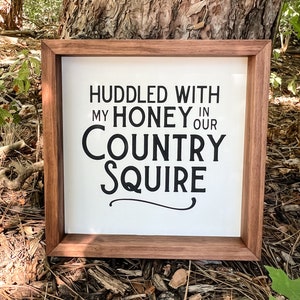 May include: A framed wood sign with white background and black text that reads "Huddled with my honey in our country squire".