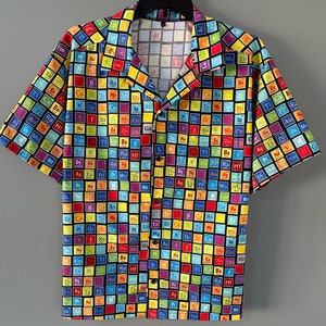 May include: Short-sleeved button-down shirt featuring a colorful periodic table design. The shirt's pattern includes various elements in a grid of squares, each with a unique color and symbol. The shirt has a classic collar and black buttons.