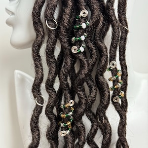 May include: Close-up of brown dreadlocks with silver and gold beaded hair rings. The rings are decorated with green and white beads.