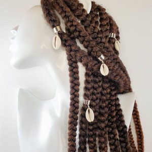 May include: Braided brown hair adorned with silver-toned metal cuffs and natural seashell charms. The braids are thick and styled, with the shells hanging from the cuffs. The hair is styled on a white mannequin head.