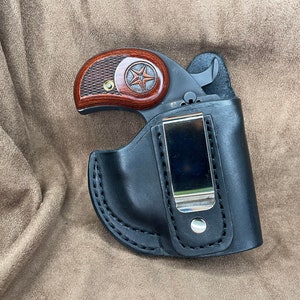 May include: A black leather holster with a silver clip for a small handgun. The holster has a brown wood handle with a star design.