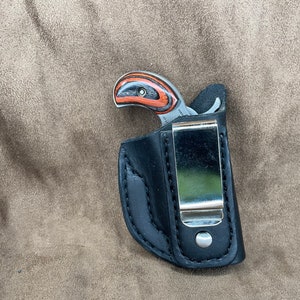 May include: A black leather holster with a silver clip for a small handgun. The handgun has a wooden grip with black and red stripes.