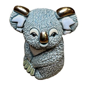 May include: A ceramic koala figurine with a textured, pale blue body and gold detailing on the ears and nose. The koala has black eyes and small, white ear patches. The figurine is a decorative item.