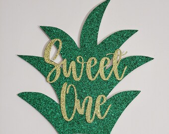 May include: Green glitter pineapple cake topper with gold glitter lettering that says "Sweet One".